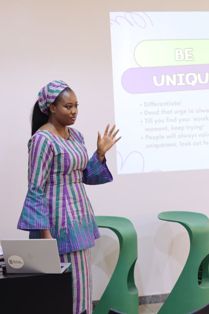 Jasmine-Jade gesturing while presenting a "Be Unique" slide at an FCDC talk